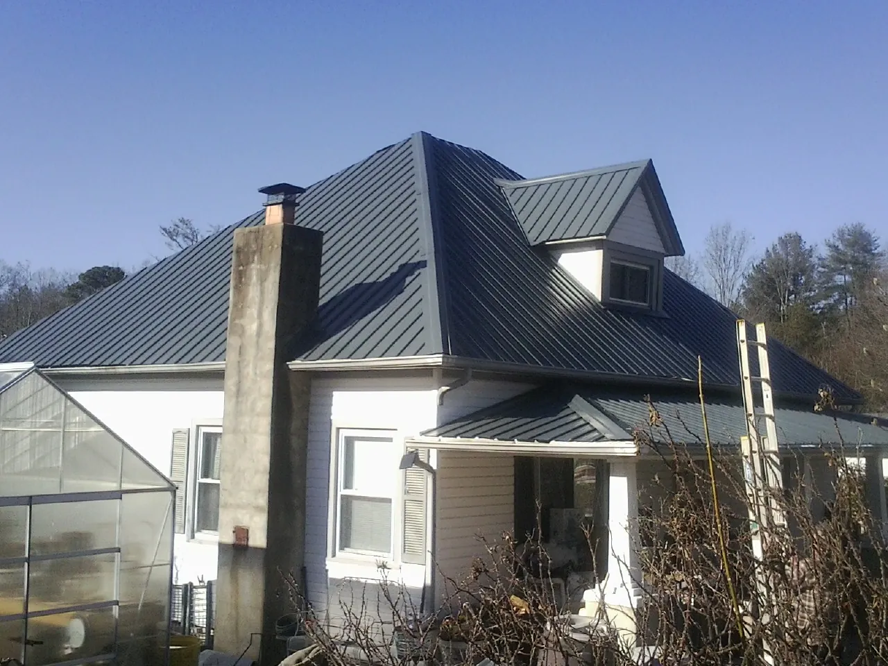 Dark blue standing seam metal roof on a white farmhouse with dormer — Slate & Tile Roof Repair by Roofing Brothers in Mc David