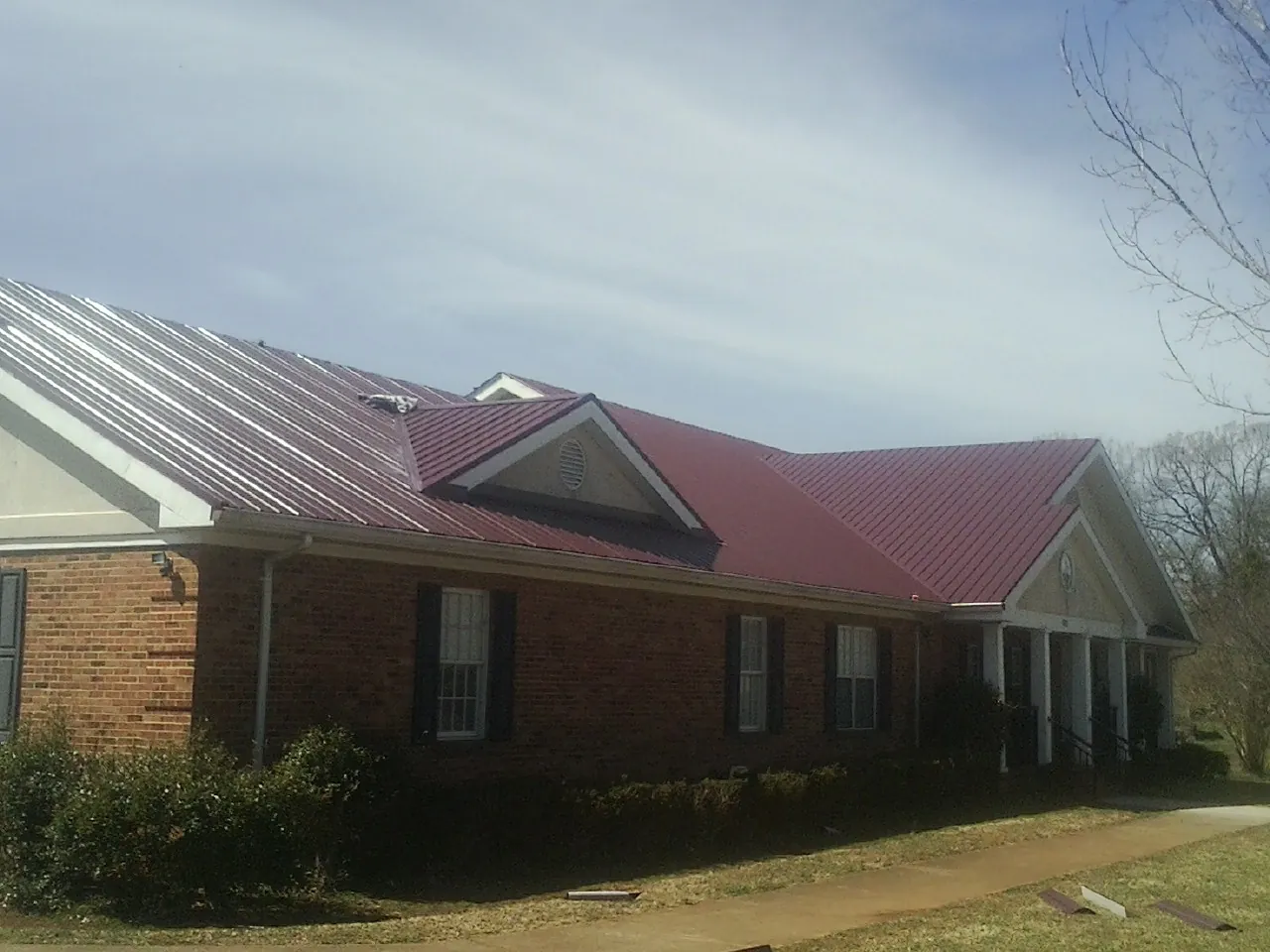Red metal roof with gabled entries on a long brick building, from a Hail Damage Roof Repair job in Mc David