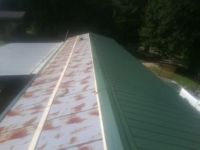Old rusted panels beside newly installed green metal roofing — Wind Damage Roof Repair by Roofing Brothers in Mc David
