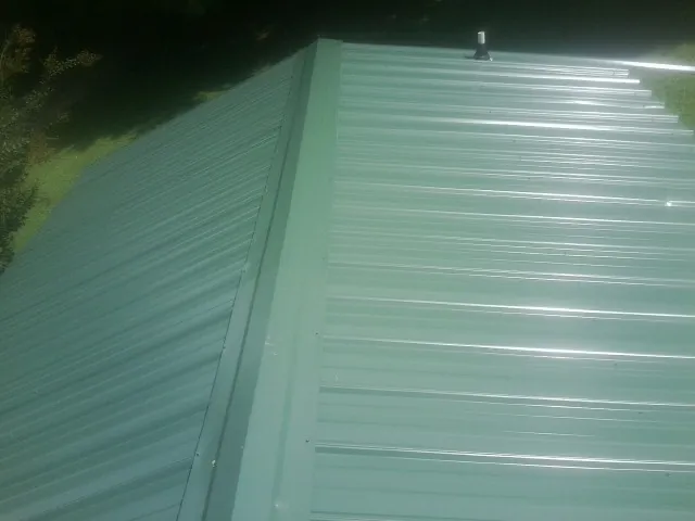 New green metal panels meeting at the ridge of a roof — Flat Roof Repair work by our crew in Mc David