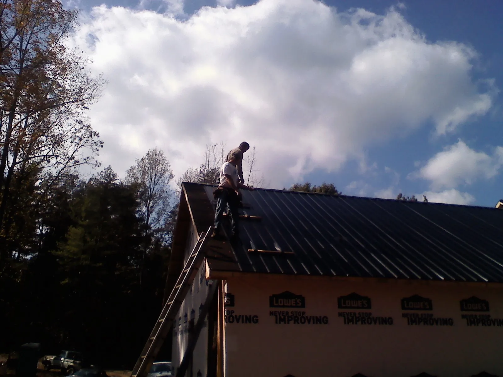 Roofer fastening dark metal panels high against a cloudy sky, from a Roof Inspection job in Mc David