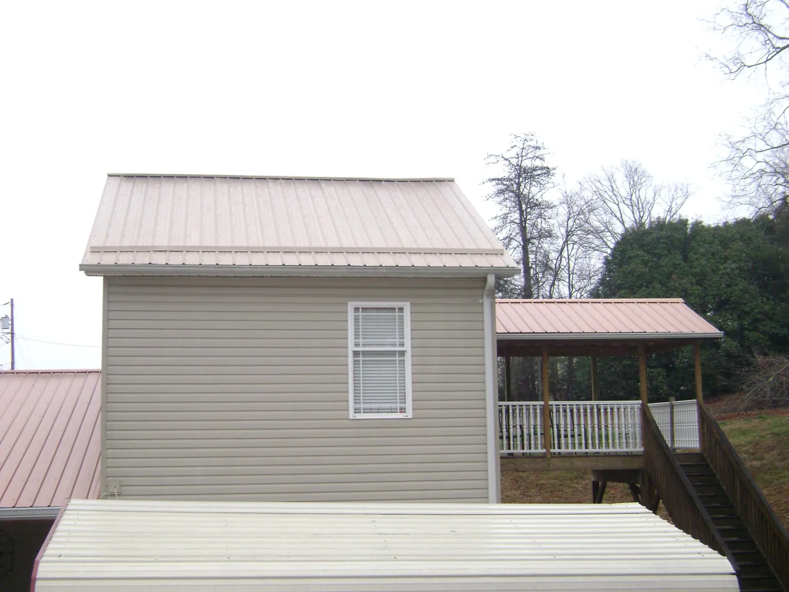 Tan metal roofs on a two story addition and attached porch, from a Roof Replacement job in Mc David